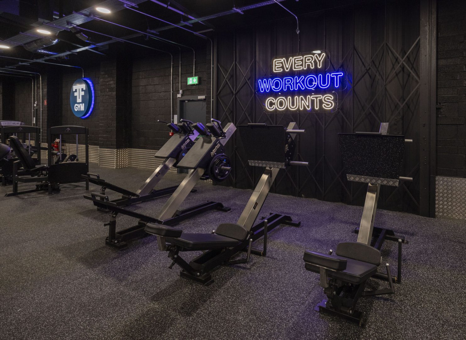 Modern gym interior with exercise machines and a neon sign saying Every Workout Counts on the black wall.